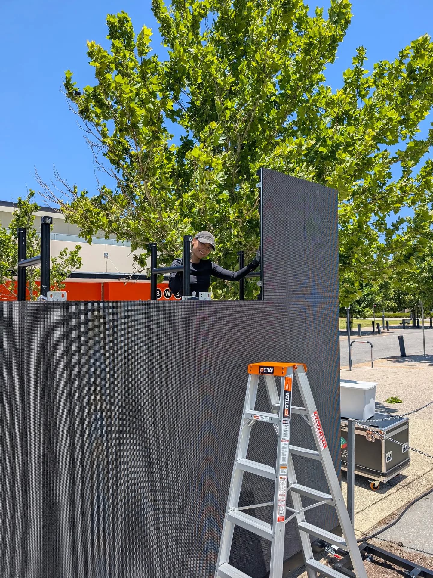 Crew member on a ladder building an LED wall panel by panel outdoors