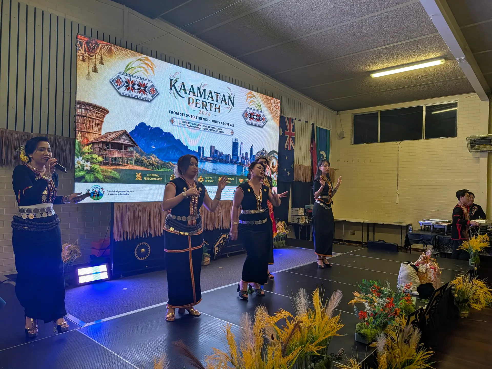 Cultural performers in traditional dress in front of an LED screen at Kaamatan
