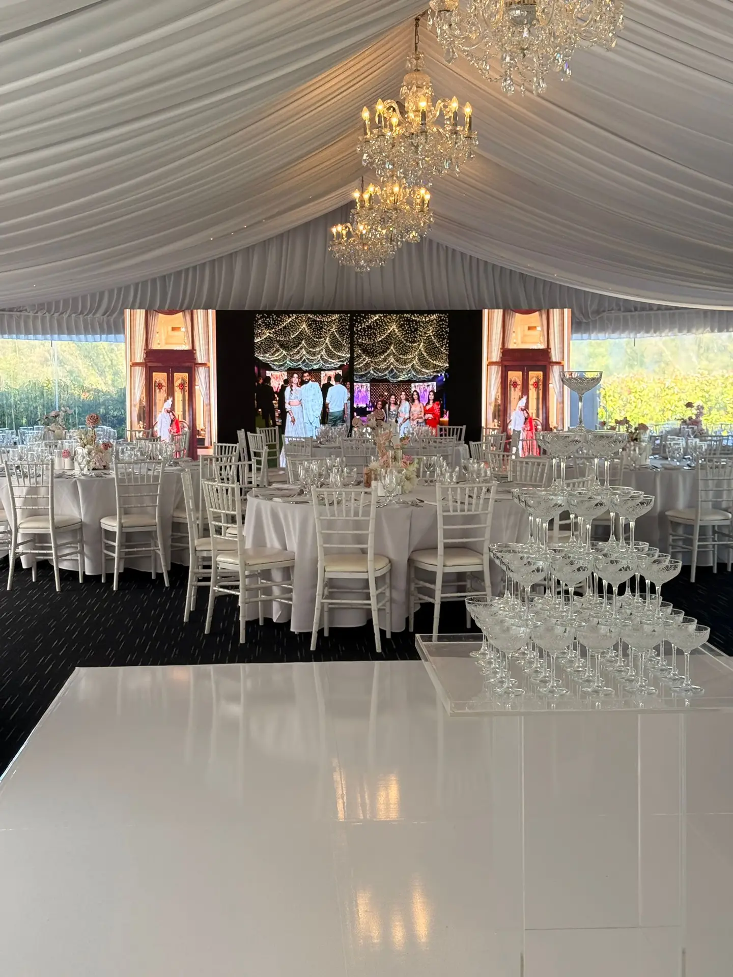 LED wall at the head of a draped wedding marquee with round tables set for dinner